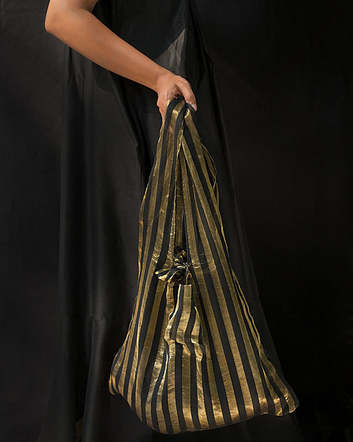 Person carrying a Raakhh Bag by its handle, in black and gold stripes.