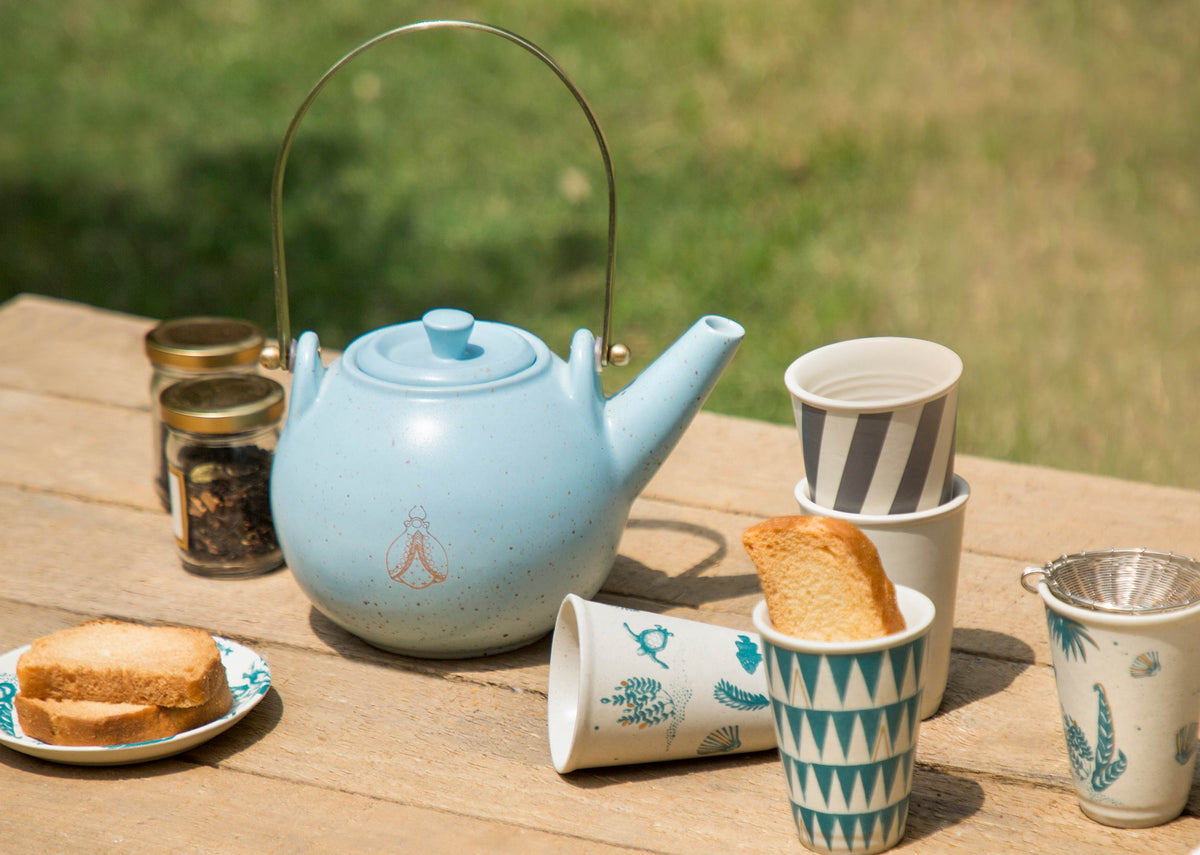 Soft blue Bug Teapot with a gold bug motif on an outdoor table.