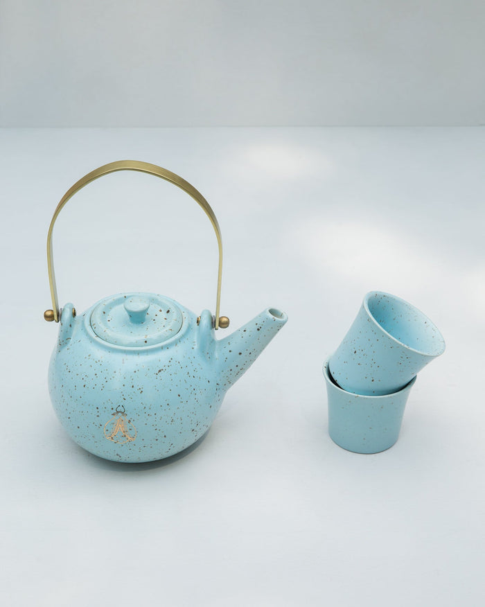 Soft blue Bug Teapot with a brass handle, shown beside two stacked cups.
