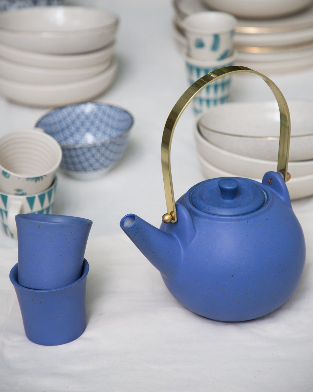 Side view of the blue Bug Teapot with a brass handle and stacked cups.