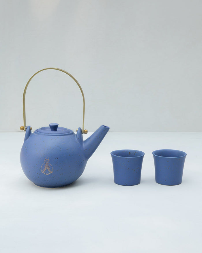 Blue Bug Teapot with a brass handle, shown beside two matching cups.