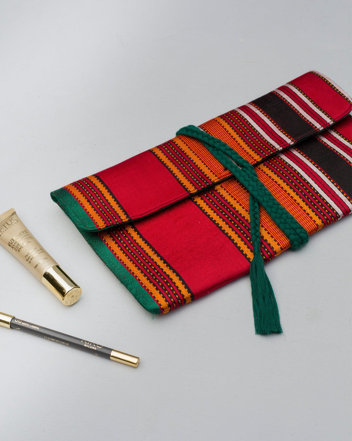 Stripe Flap Clutch lying flat with its green braided tie across the front.