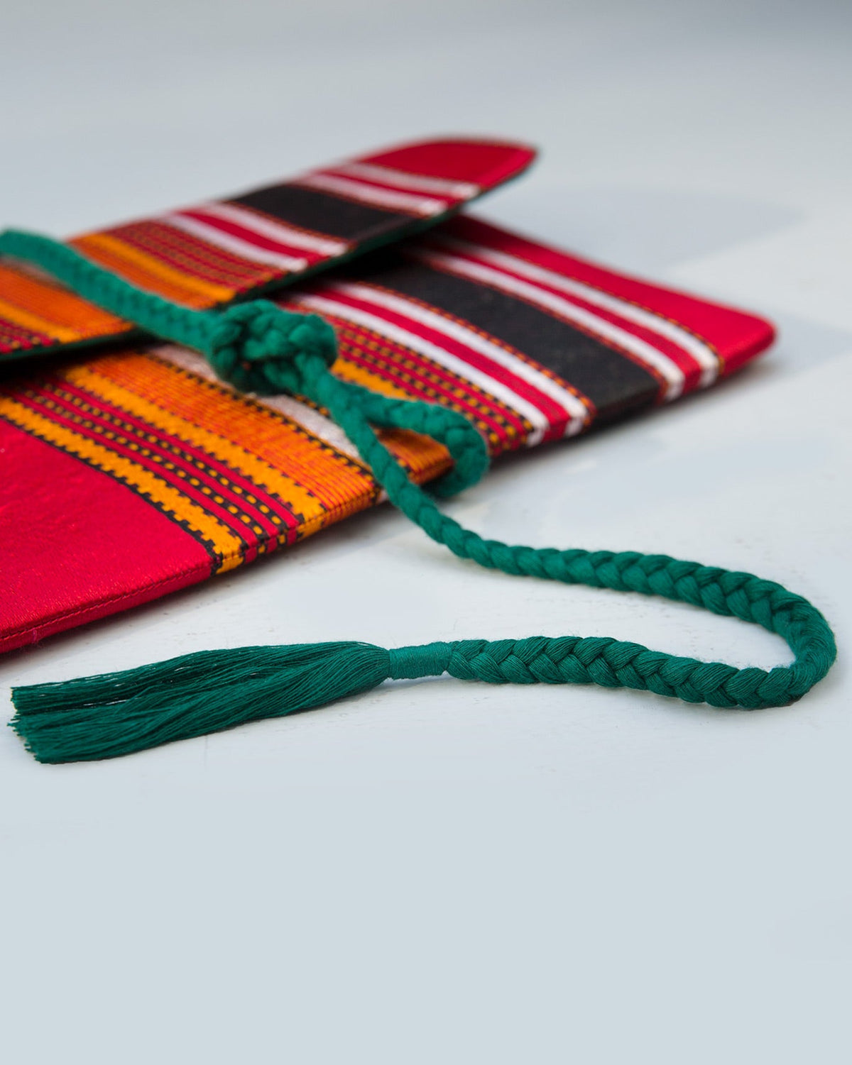Close-up of Stripe Flap Clutch's green braided tie and tassel.