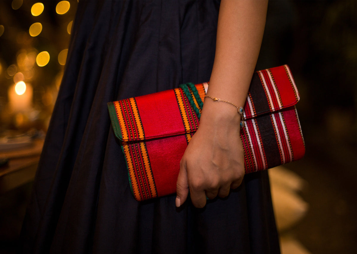 Person holding a Stripe Flap Clutch at the hip, in red woven stripes.