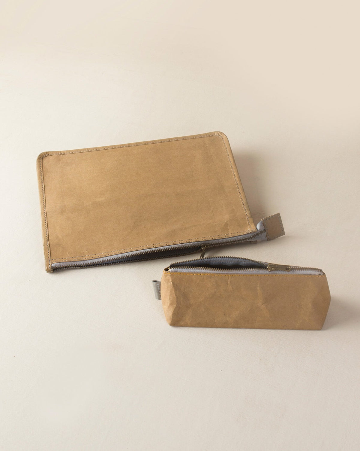 Brown Planet First Paper Pouches lying flat, with grey zips.