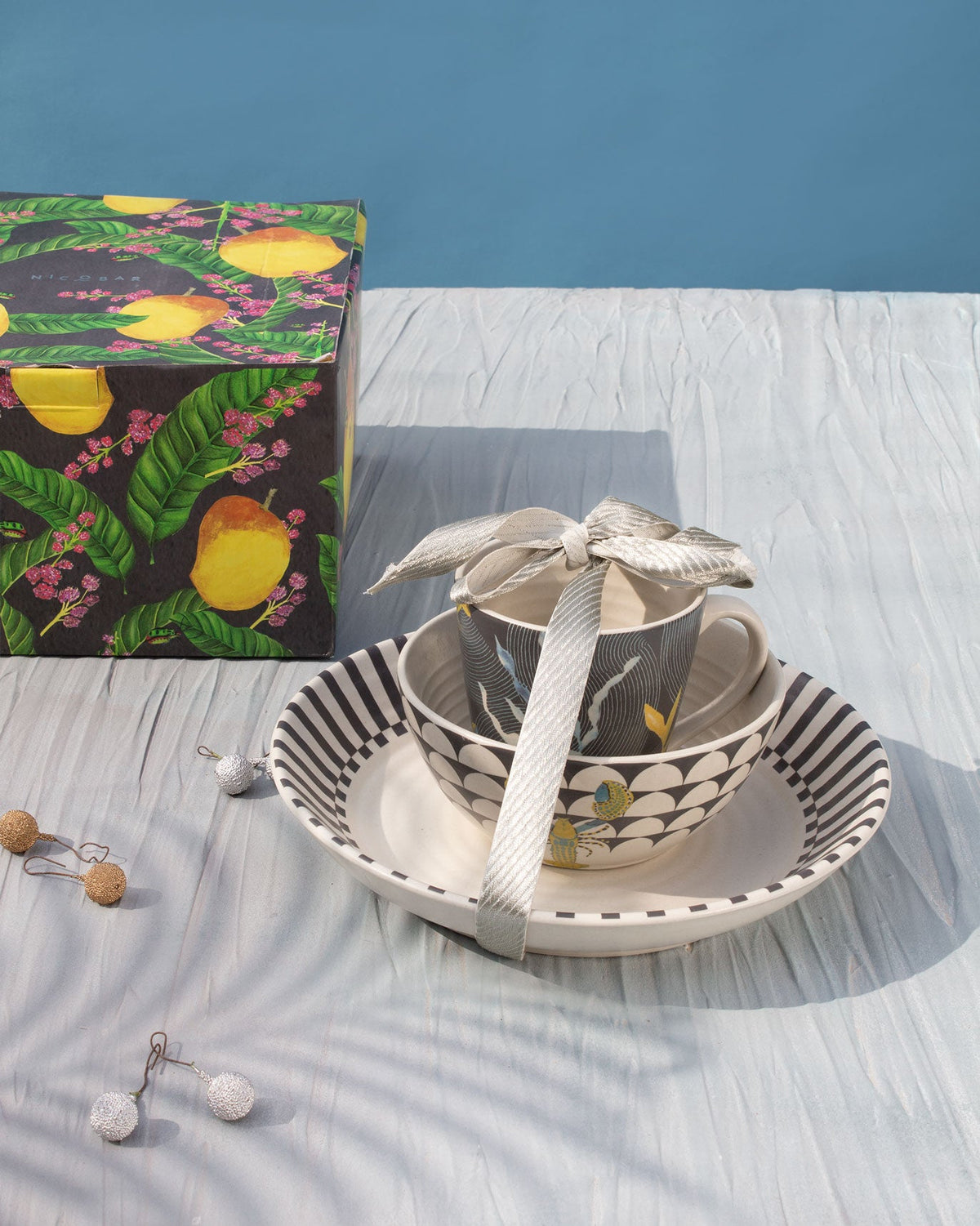 Champa Breakfast Set tied with a ribbon, set on a striped plate beside a lemon-print box.