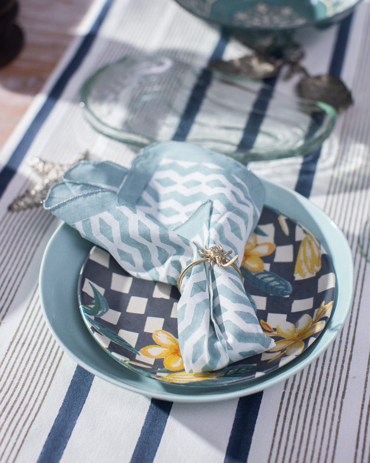 Allamanda Dinner Napkin folded into a bundle in a teal chevron print.