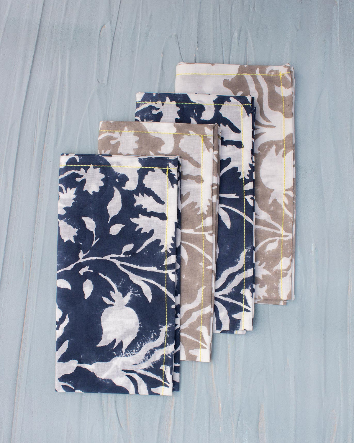 Four Cardinal Dinner Napkins layered in navy and taupe floral prints.