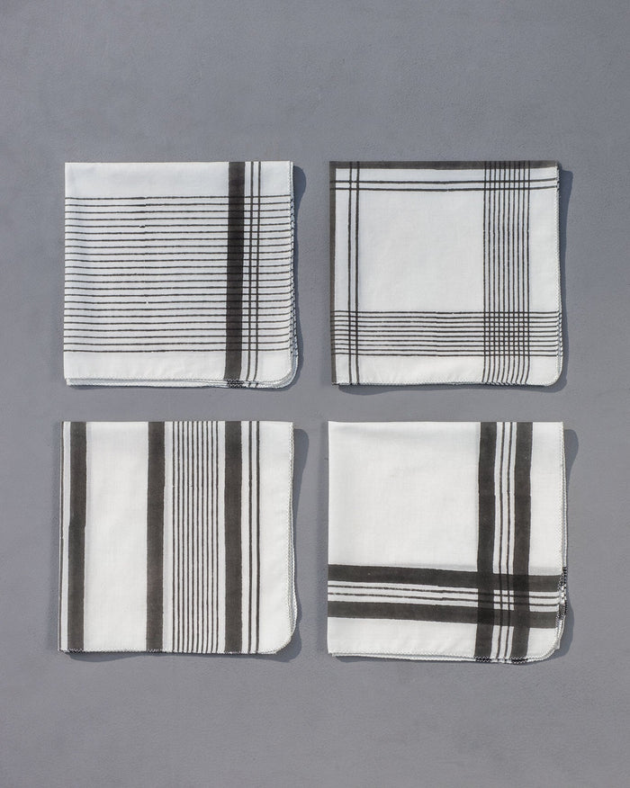 Set of four Stone Town dinner napkins laid in a grid on a grey surface.