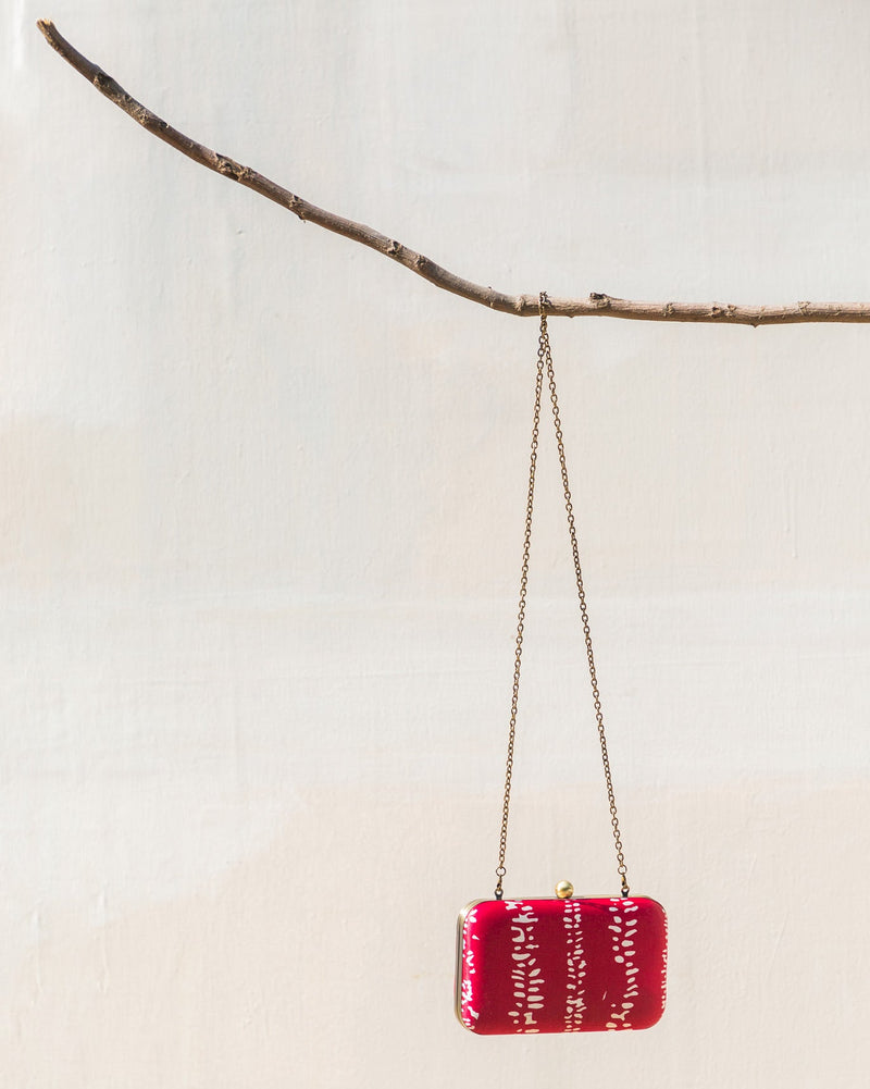 Martini Clutch in red with a white dashed pattern, hanging from a branch.
