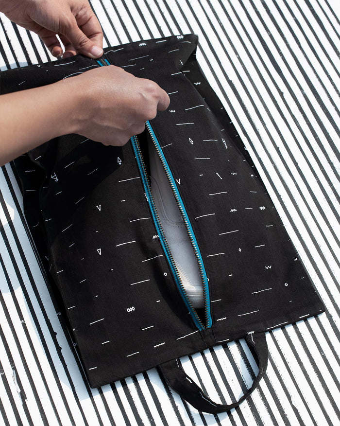 Person unzipping a black Musafir shoe sack to show a shoe inside.