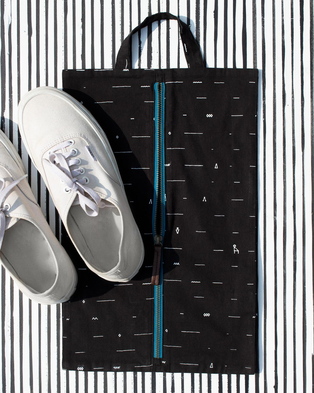 Black Musafir shoe sack laid flat, with a pair of white sneakers beside it.