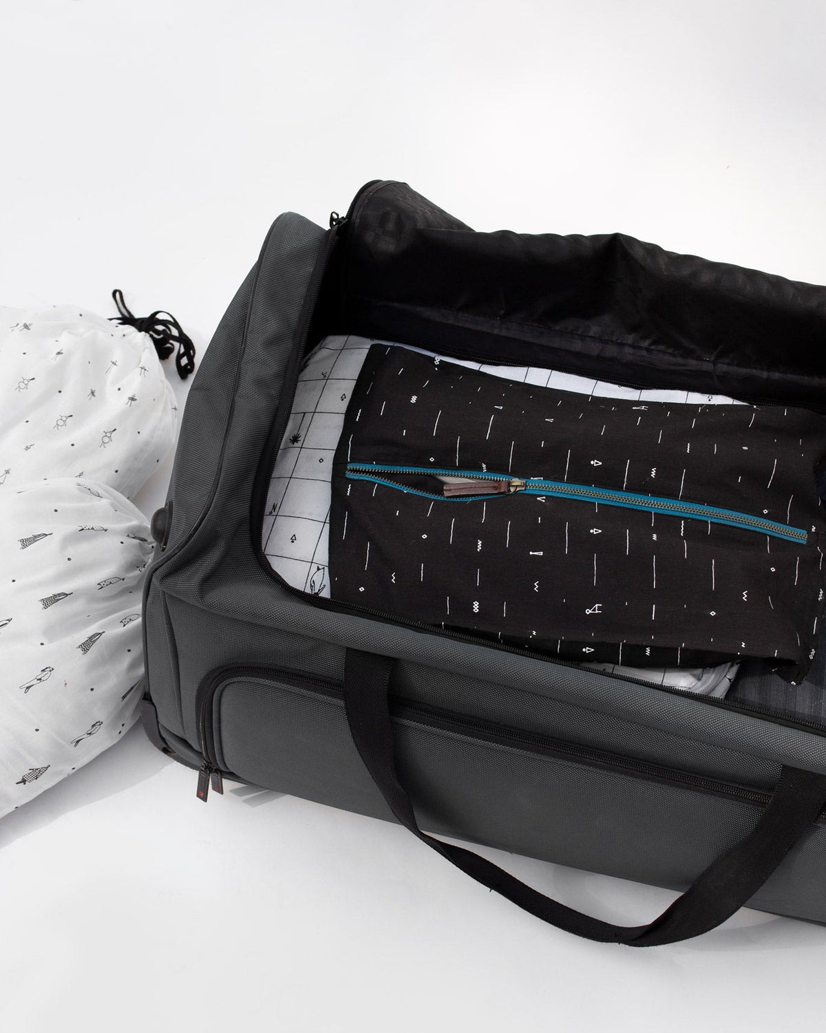Black Musafir shoe sack resting beside an open suitcase.