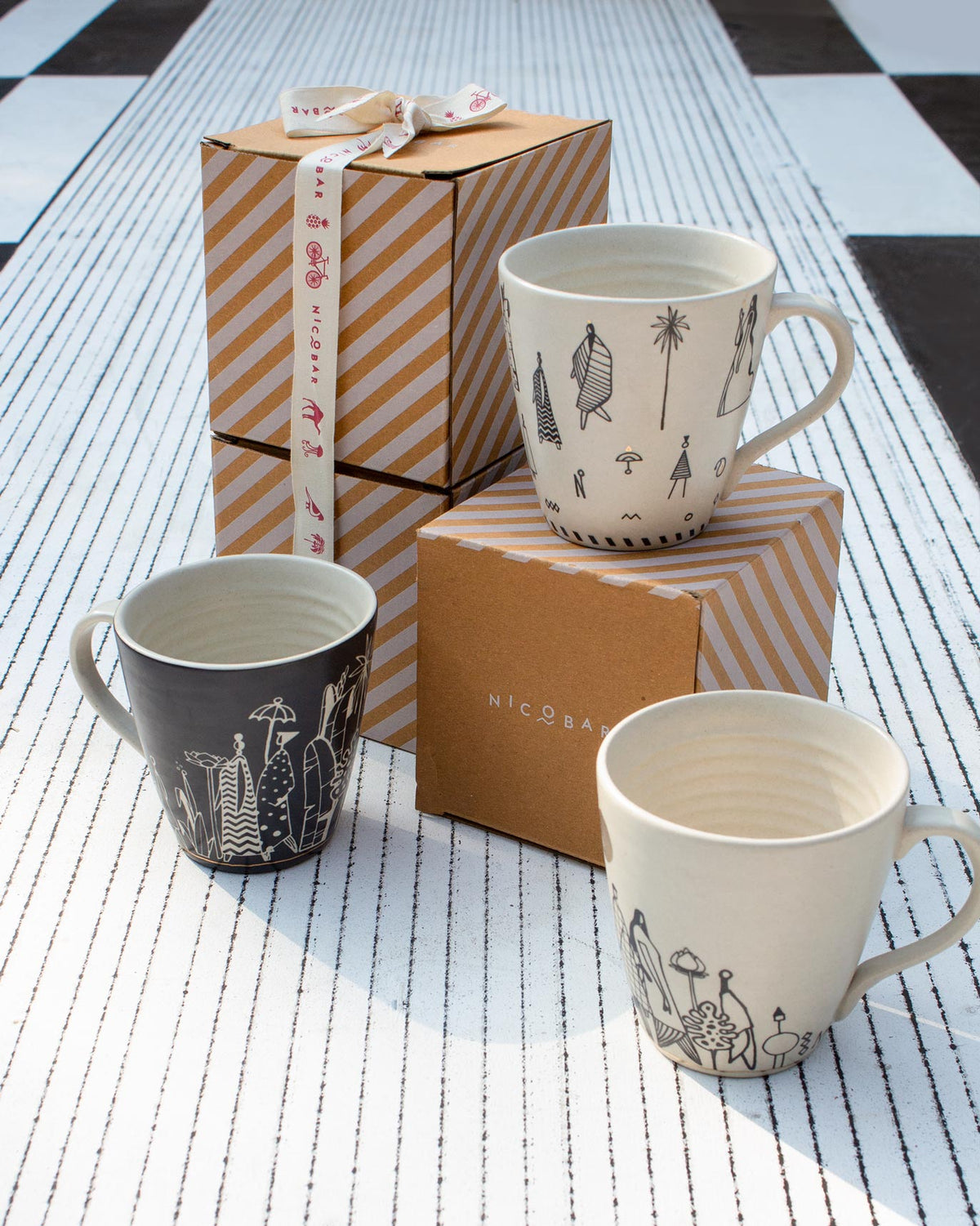 Musafir Mug with black figure drawings, grouped with other mugs and gift boxes.