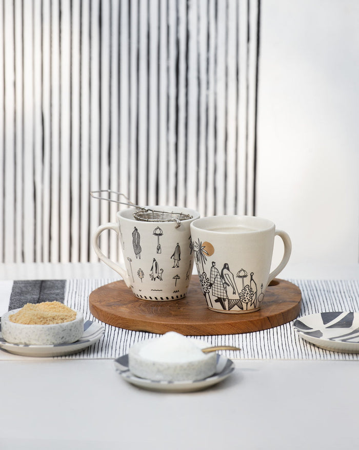 White Tribe Mug with black line figures on a wooden board beside another mug.