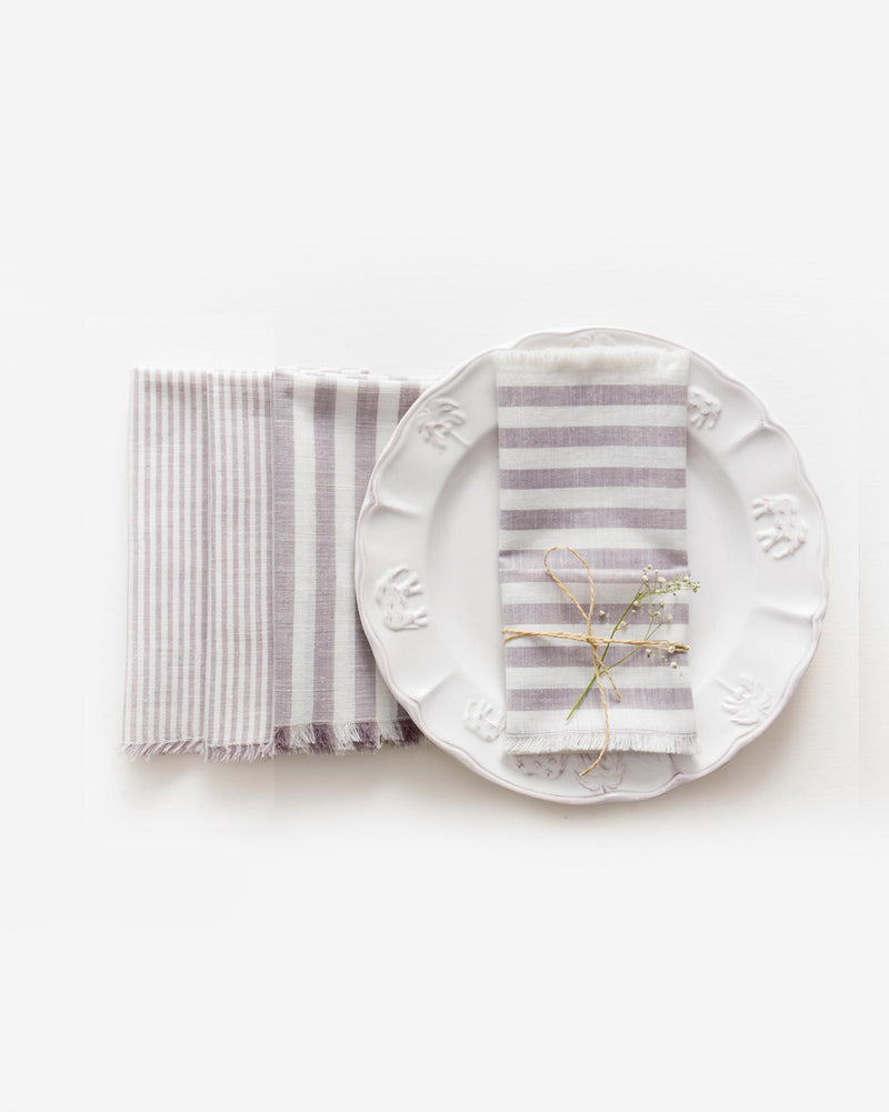 Overhead view of Alleppey Dinner Napkins in grey stripes, one folded on a white plate.