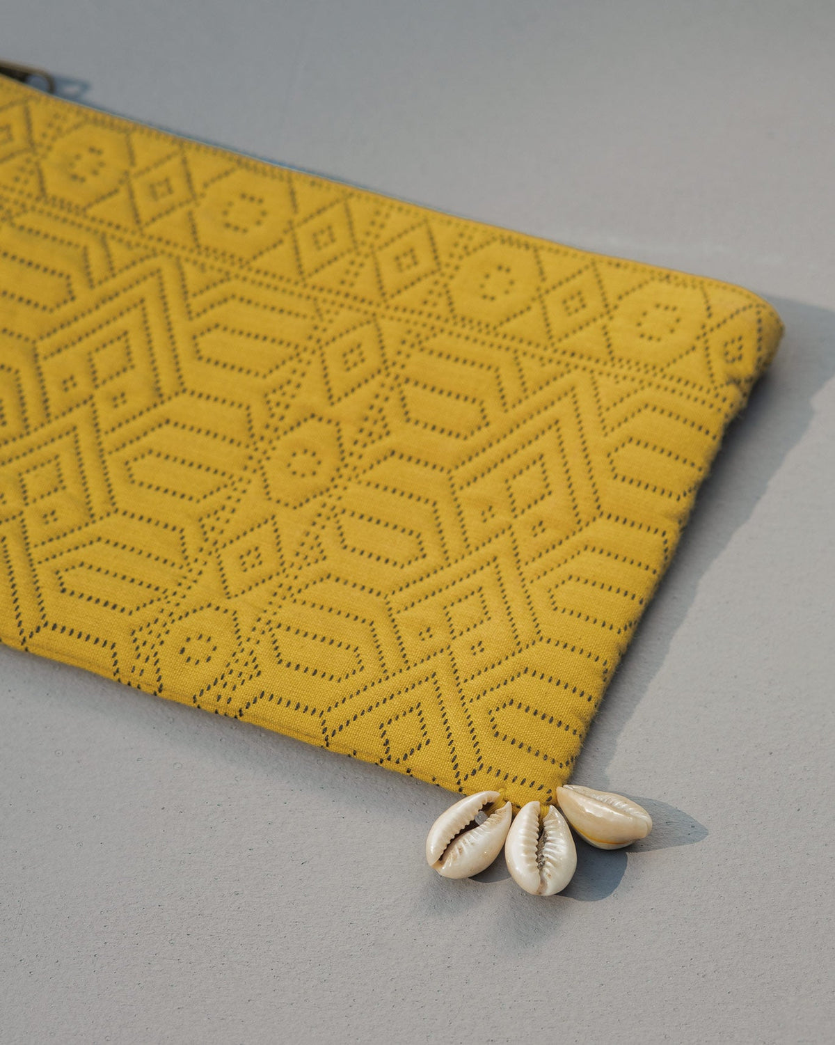 Corner of the Midi Jacquard Pouch with three cowrie shells at the tip.