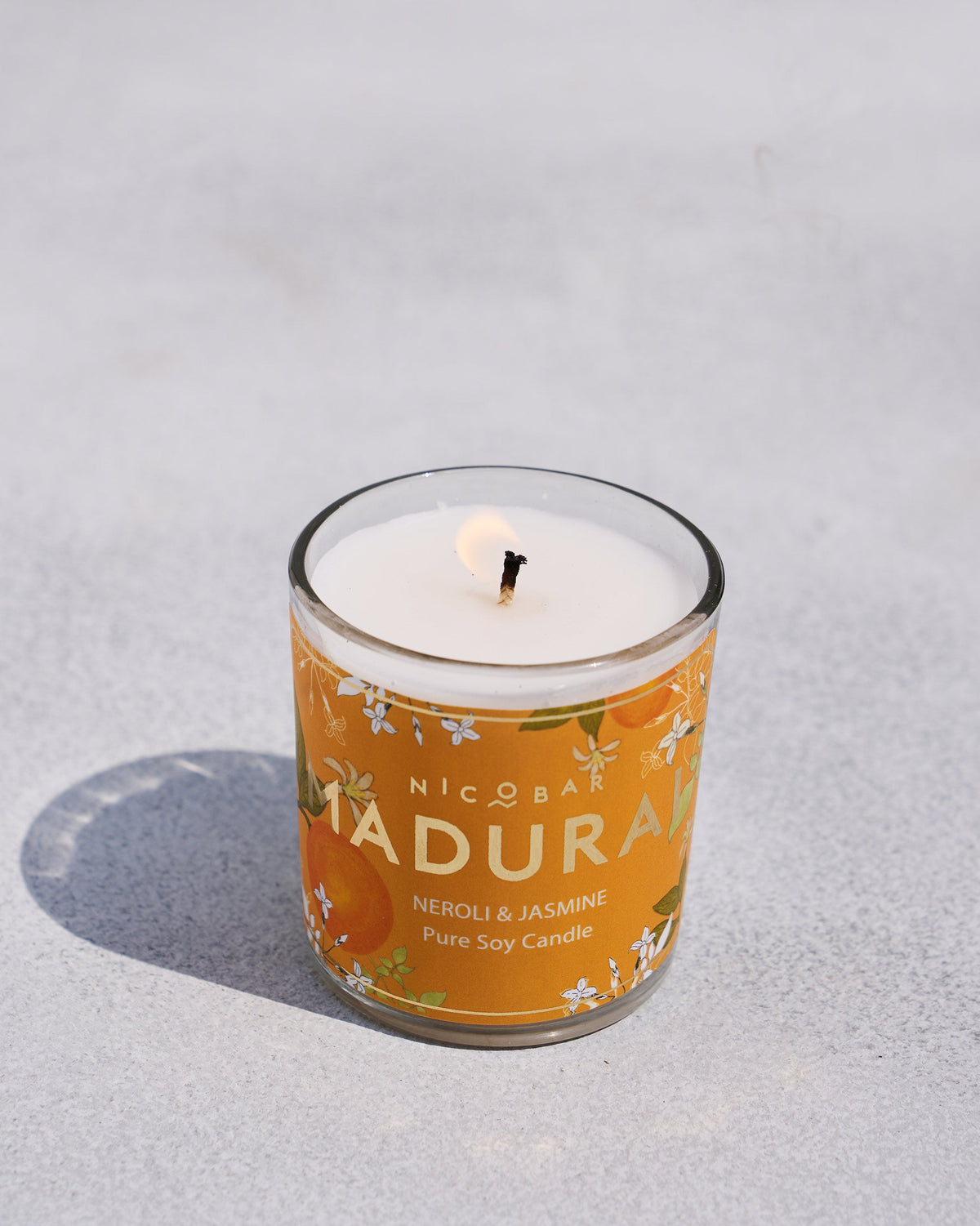 Lit Madurai jar candle in a glass with an orange label.