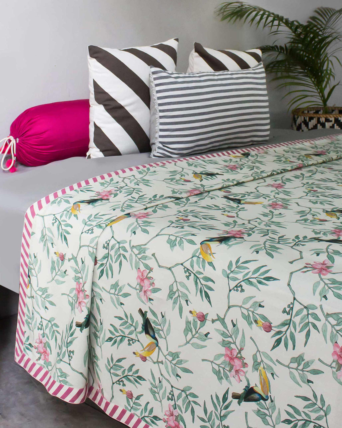 Ivory Nakano bed cover with toucan print and a pink diagonal striped border.