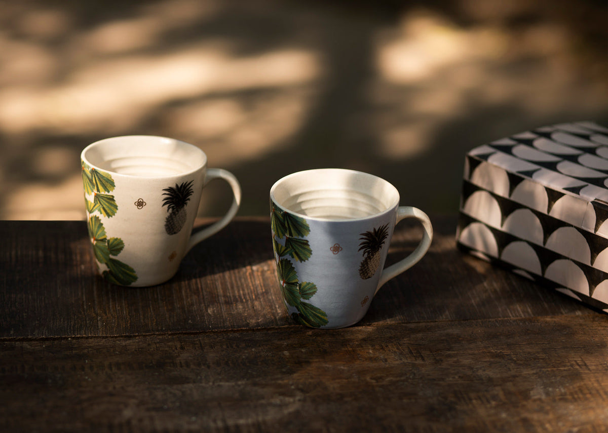 Oyster Bay Mug Set on a wooden table, with small pineapple and leaf designs.
