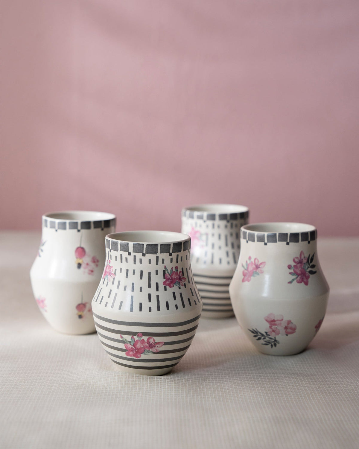Four Nectar Kulhars standing in a row, with pink flower and stripe motifs.