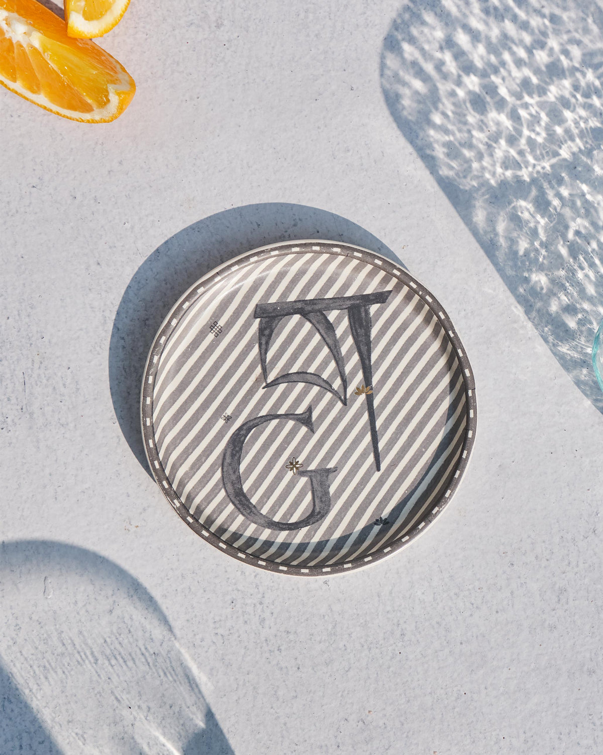 Akshar Coaster with a letter G on grey diagonal stripes.