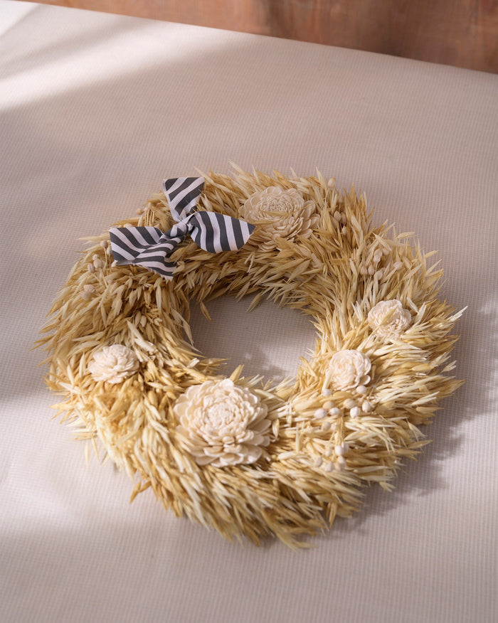Lumi Wreath with pale dried grass, cream flower heads and a grey striped bow.