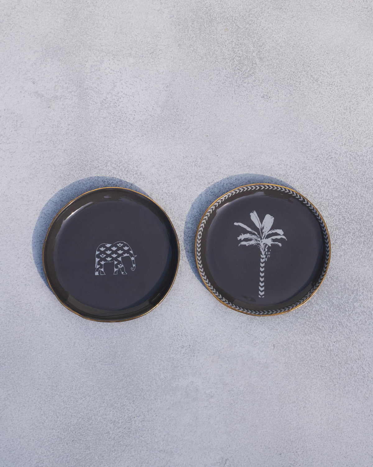 Pair of Coastal Tea Plates in charcoal laid flat, one with an elephant and one with a palm.