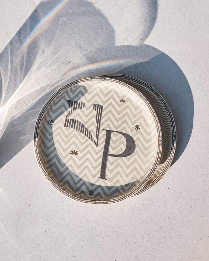 Akshar Coaster with a letter P on a grey chevron pattern, seen at an angle.