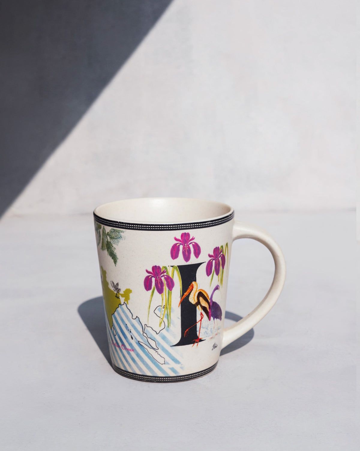 Imli mug with purple irises and a long-legged bird beside a large black letter.