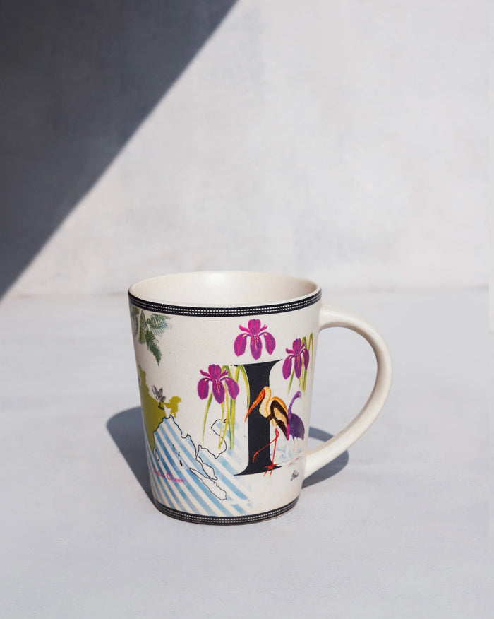 Imli mug with purple irises and a long-legged bird beside a large black letter.