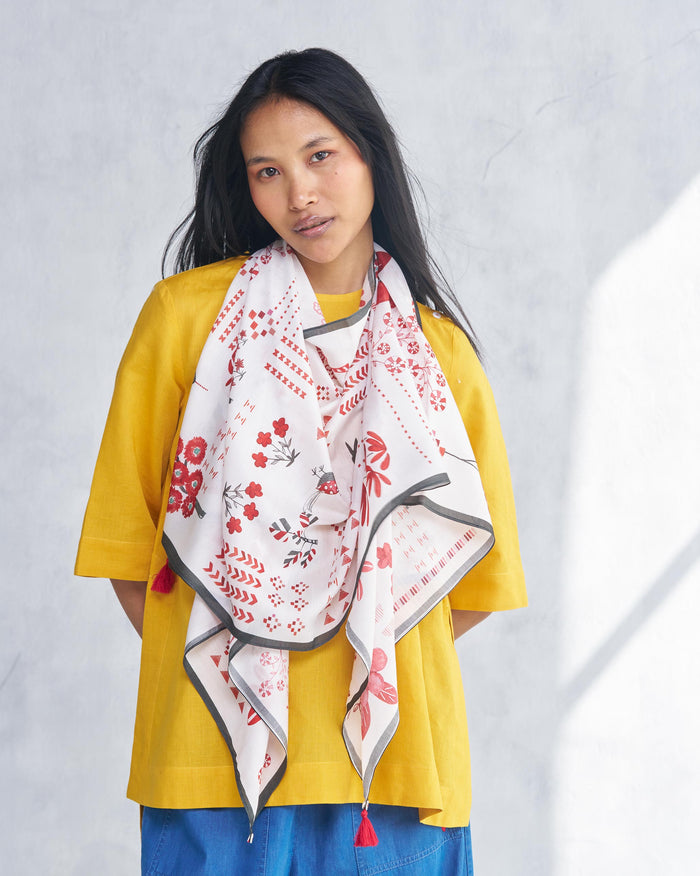 Person wearing a white Sugato scarf with red floral and geometric motifs.