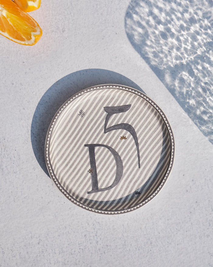 Akshar Coaster with a large letter D on grey diagonal stripes.