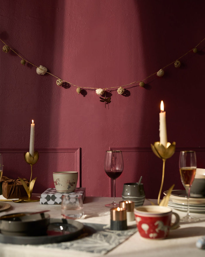 Lumi Toran garland with woven balls, dried pods and gold thread, strung across a wall.