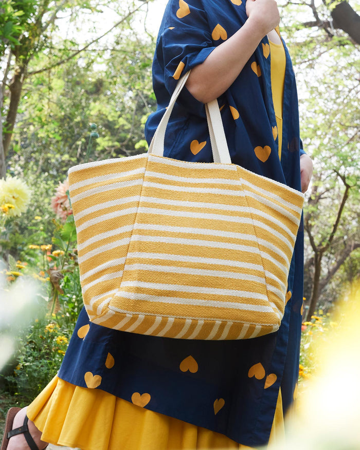 Person carrying a yellow and ivory striped Sunrise Stripe Tote on the shoulder.