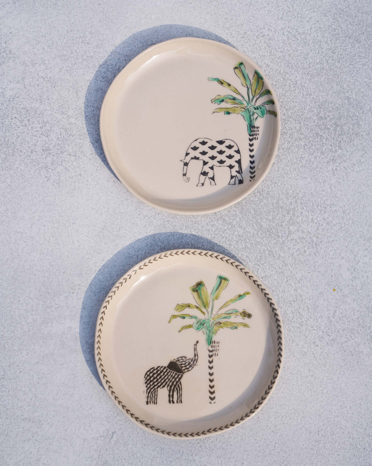 Pair of ivory coastal tea plates with elephant and palm prints, one with a chevron rim.