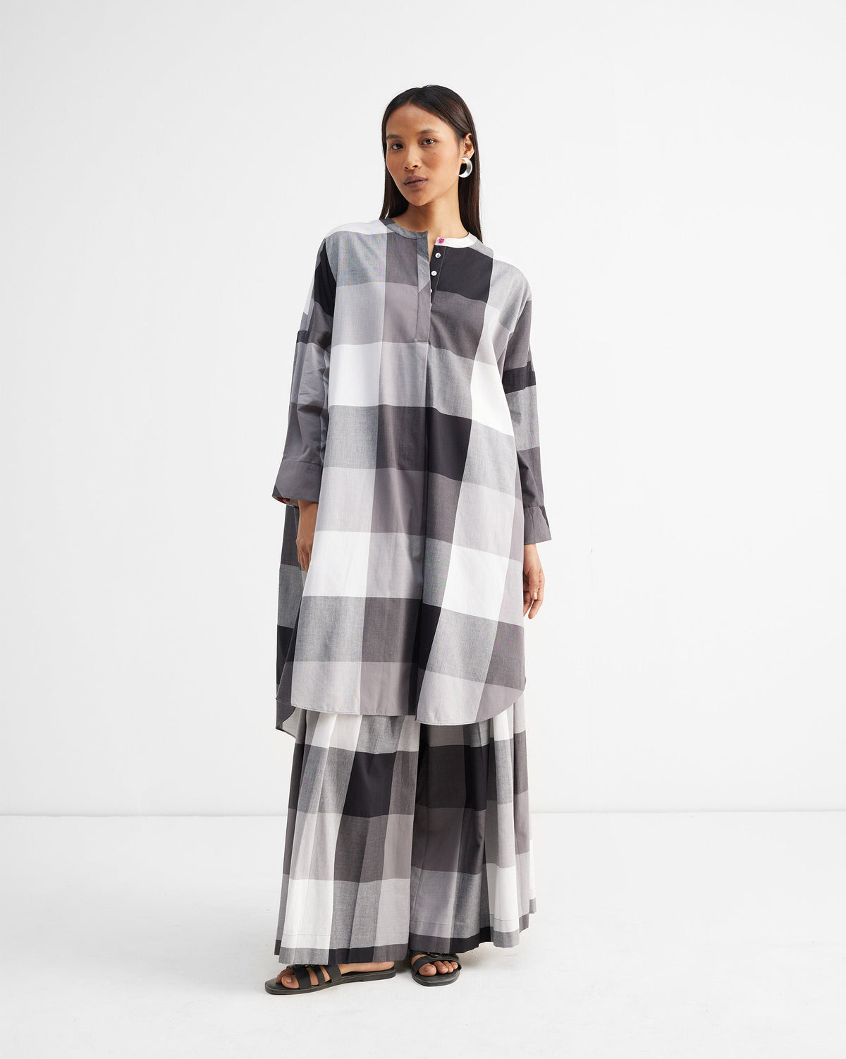 Person wearing black and white checked Pleated Trousers under a long top.