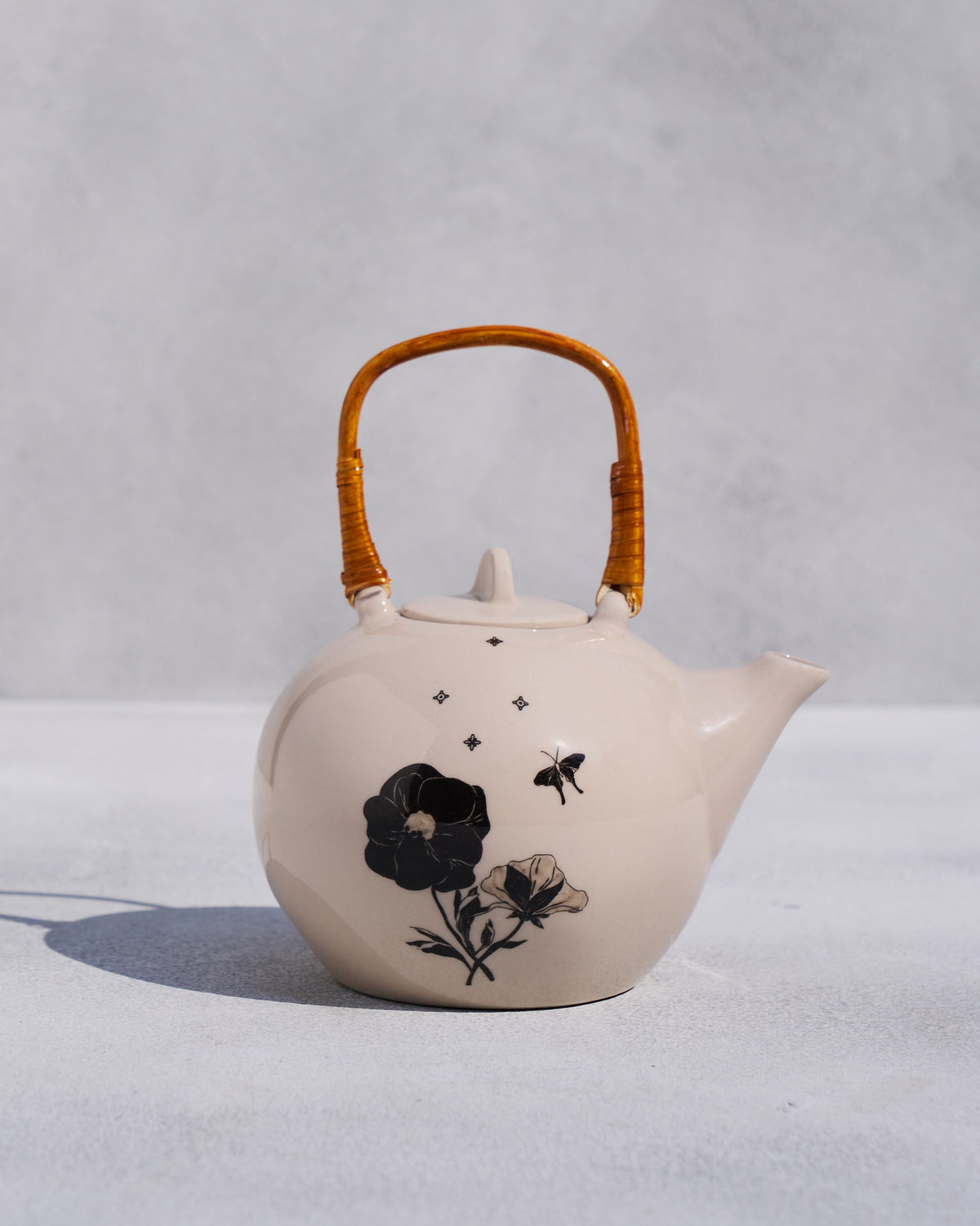 Ivory Poppy teapot with rattan handle and black poppy illustrations.