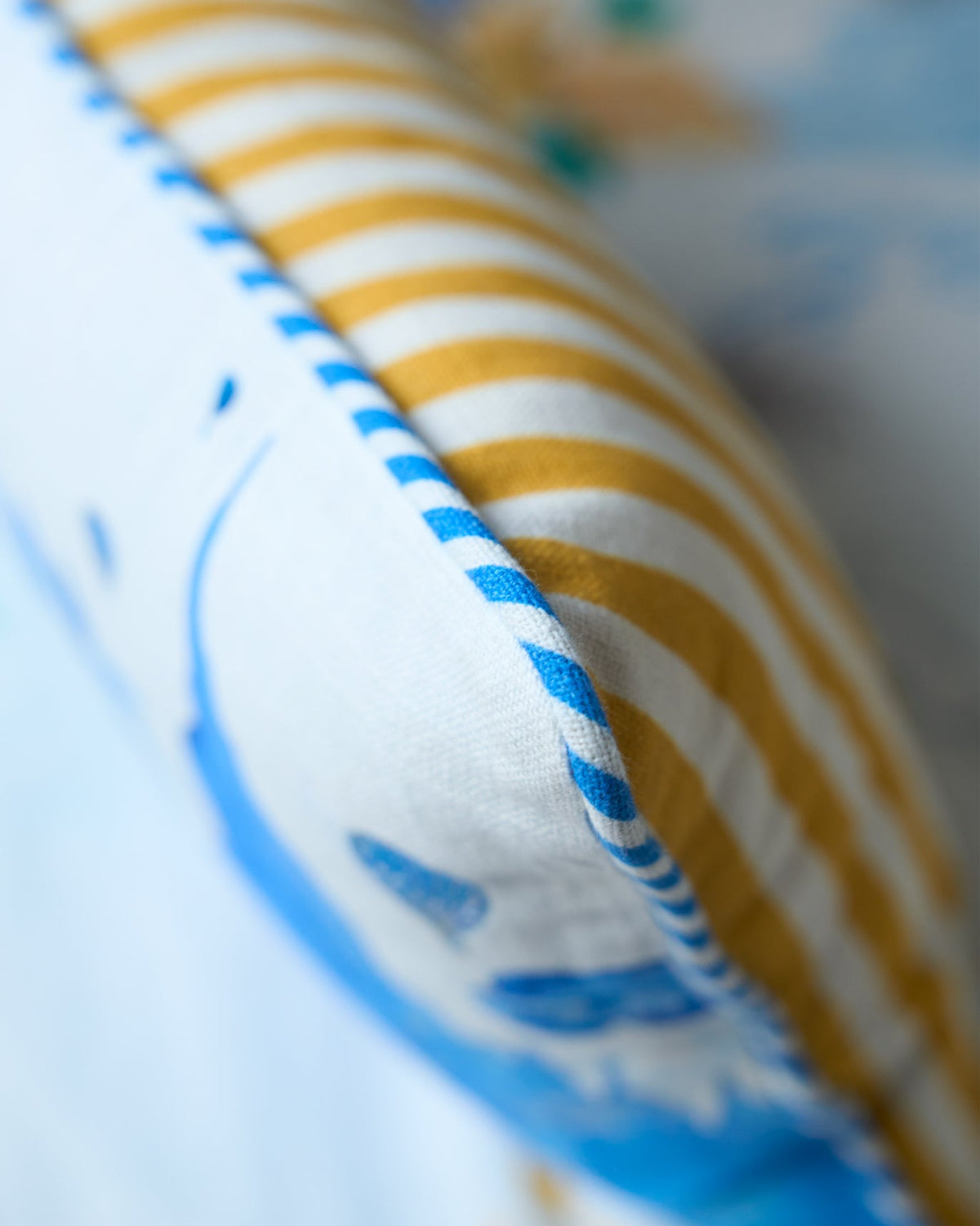 Close-up of the Caravan Cushion Cover edge showing mustard stripes and blue piping.