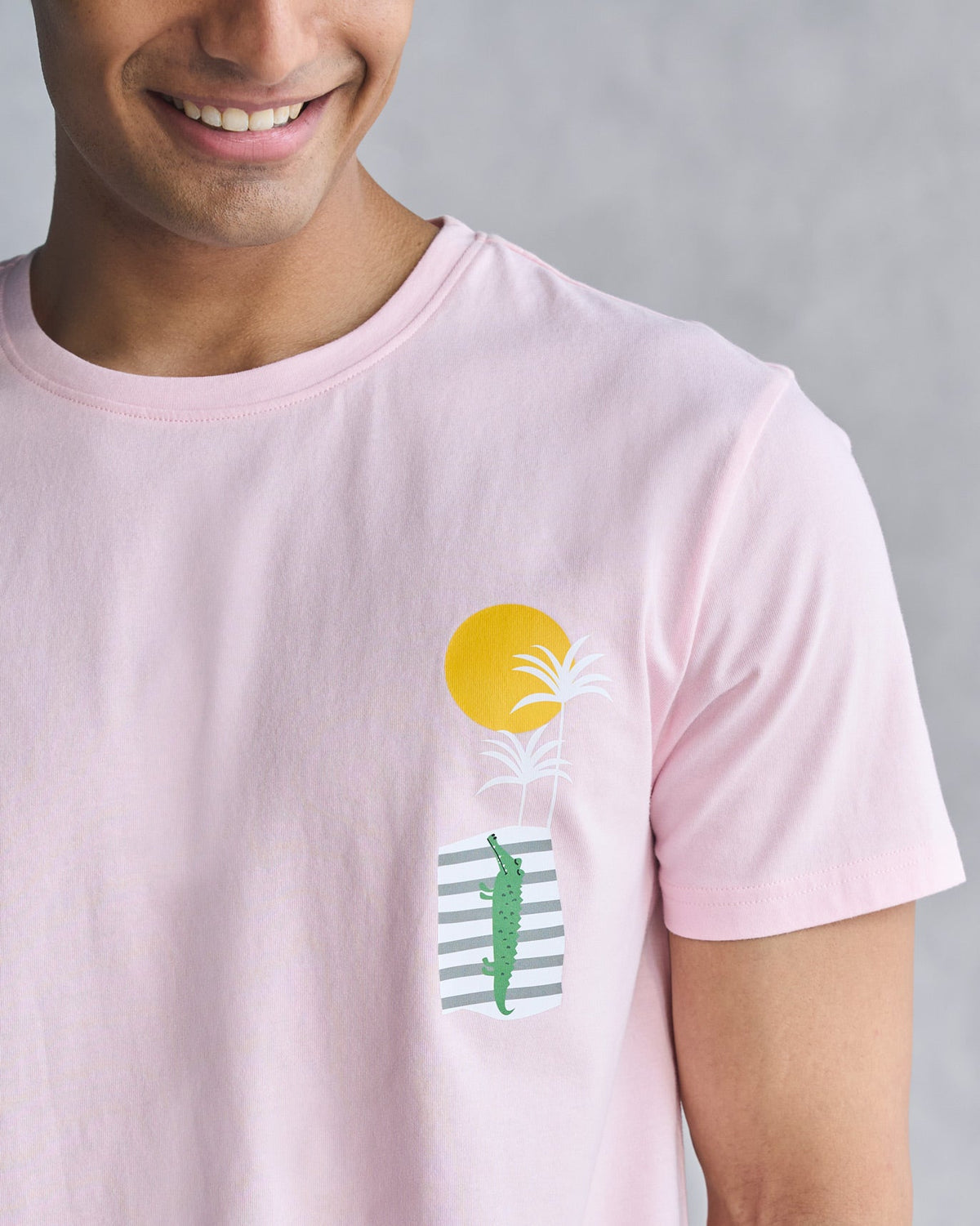 Close-up of a soft pink t-shirt showing a yellow sun, palm fronds and a green alligator print.