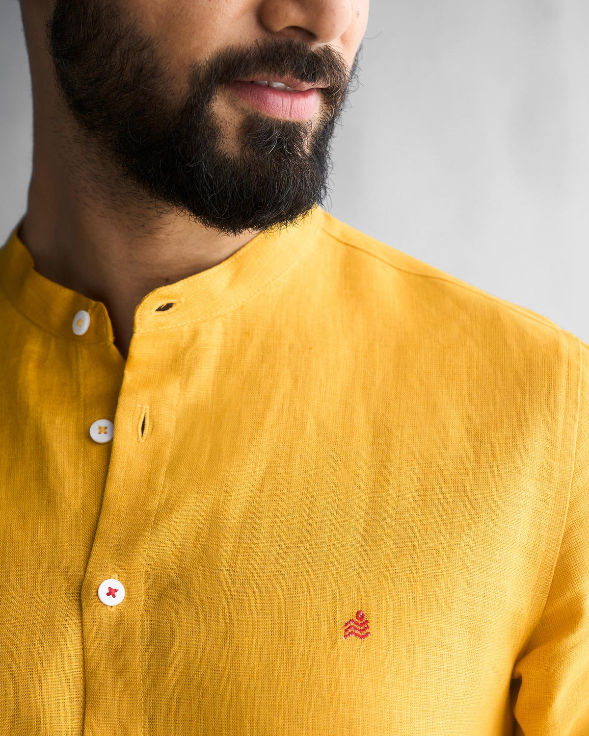 Close-up of an ochre Nawab shirt placket showing a small red embroidered logo.