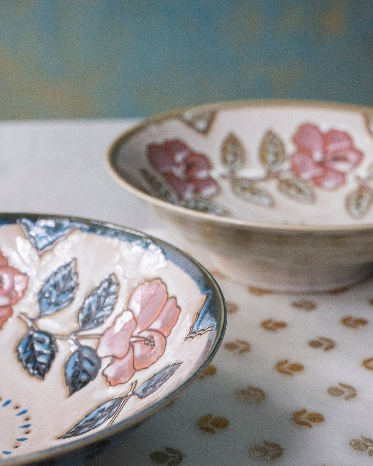 Close-up of a Moor Shallow Bowl with pink flowers and blue leaves on its rim.