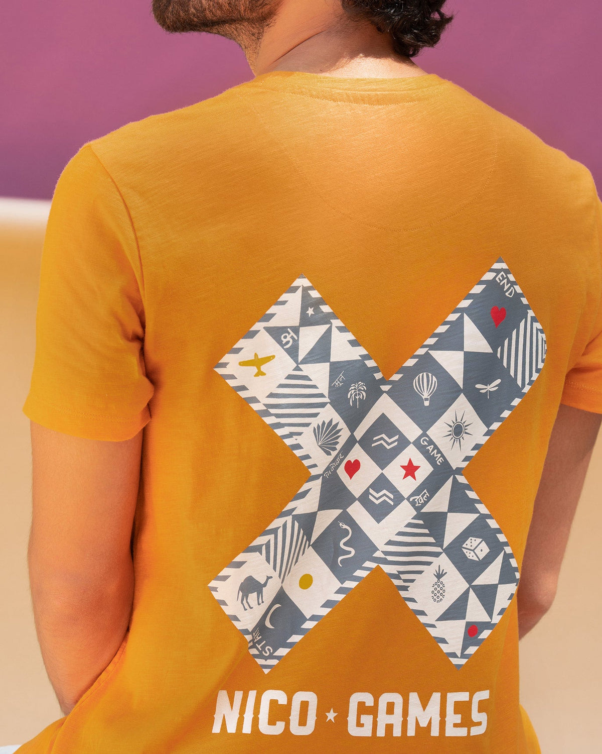Back of an orange Roll the Dice t-shirt with a large printed X and NICO GAMES text.