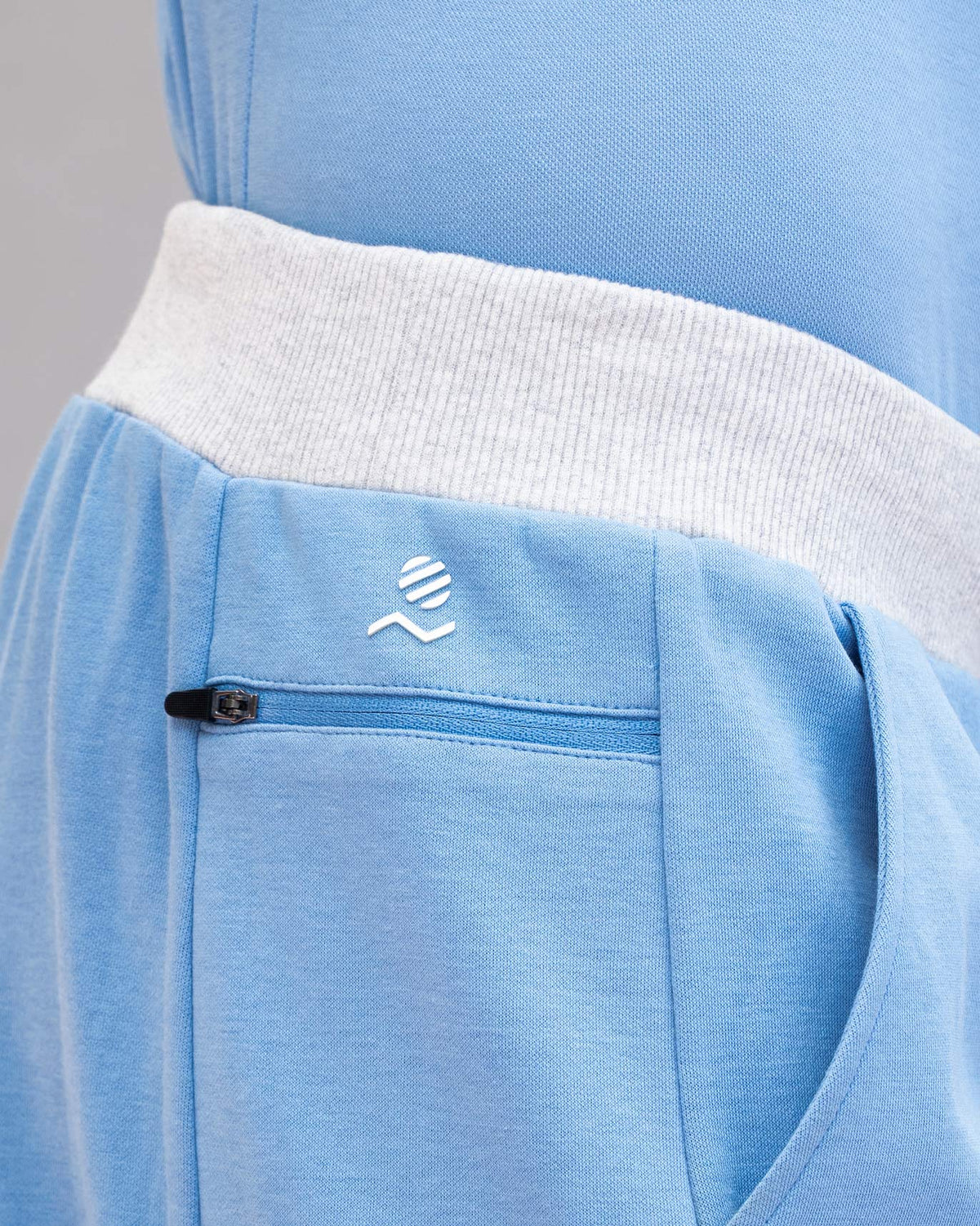 Close-up of blue Rally training shorts showing a zip pocket and white logo.