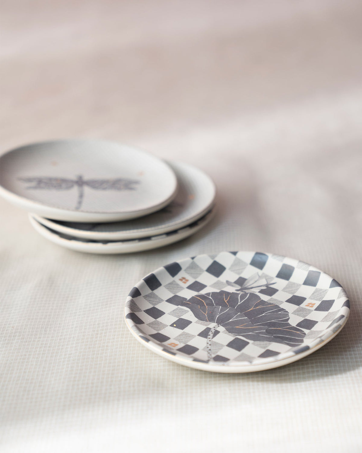 Nectar tea plates stacked behind a checkered plate with a large grey motif.