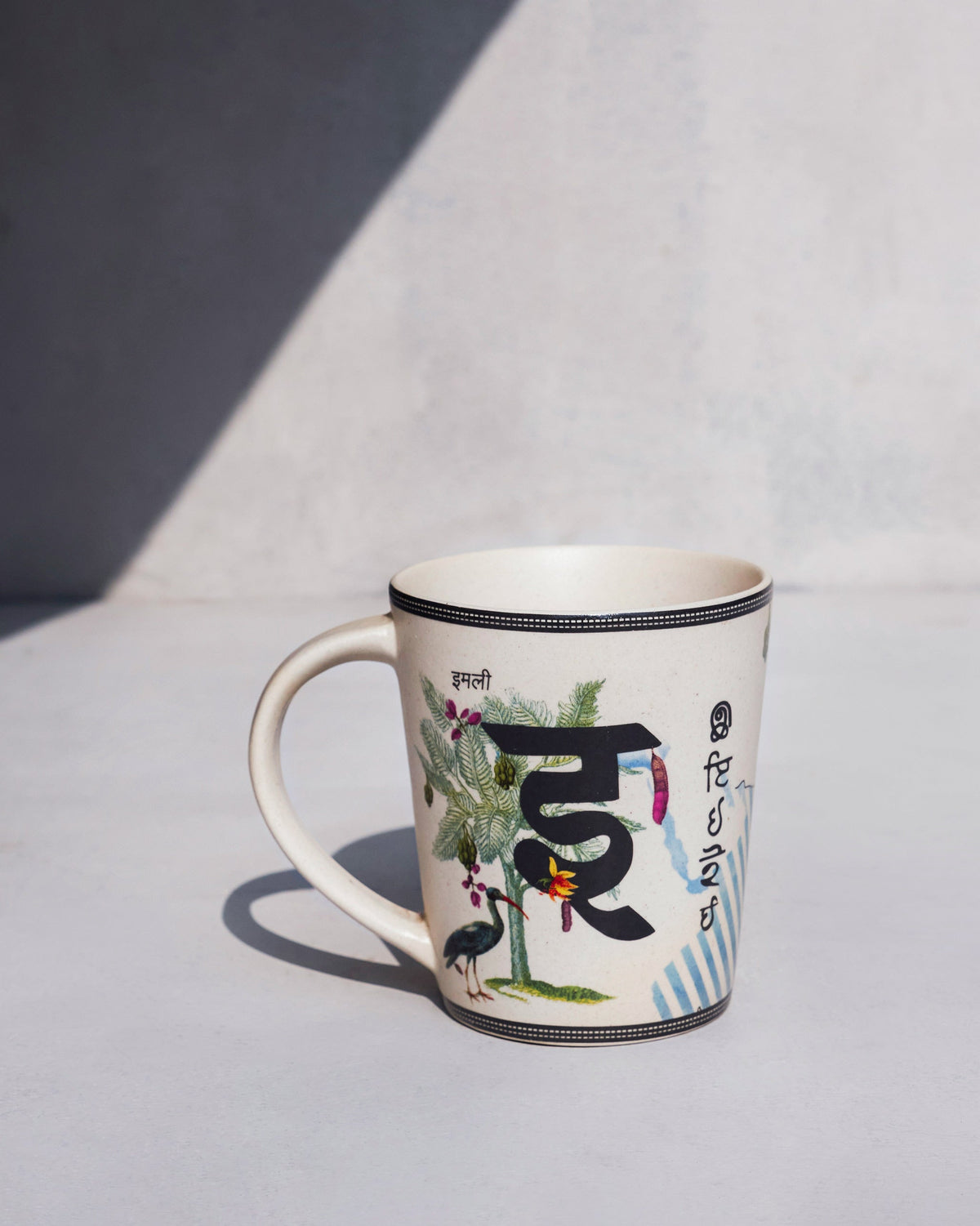 Imli mug with a Hindi word, a leafy tree and a bird printed on its side.