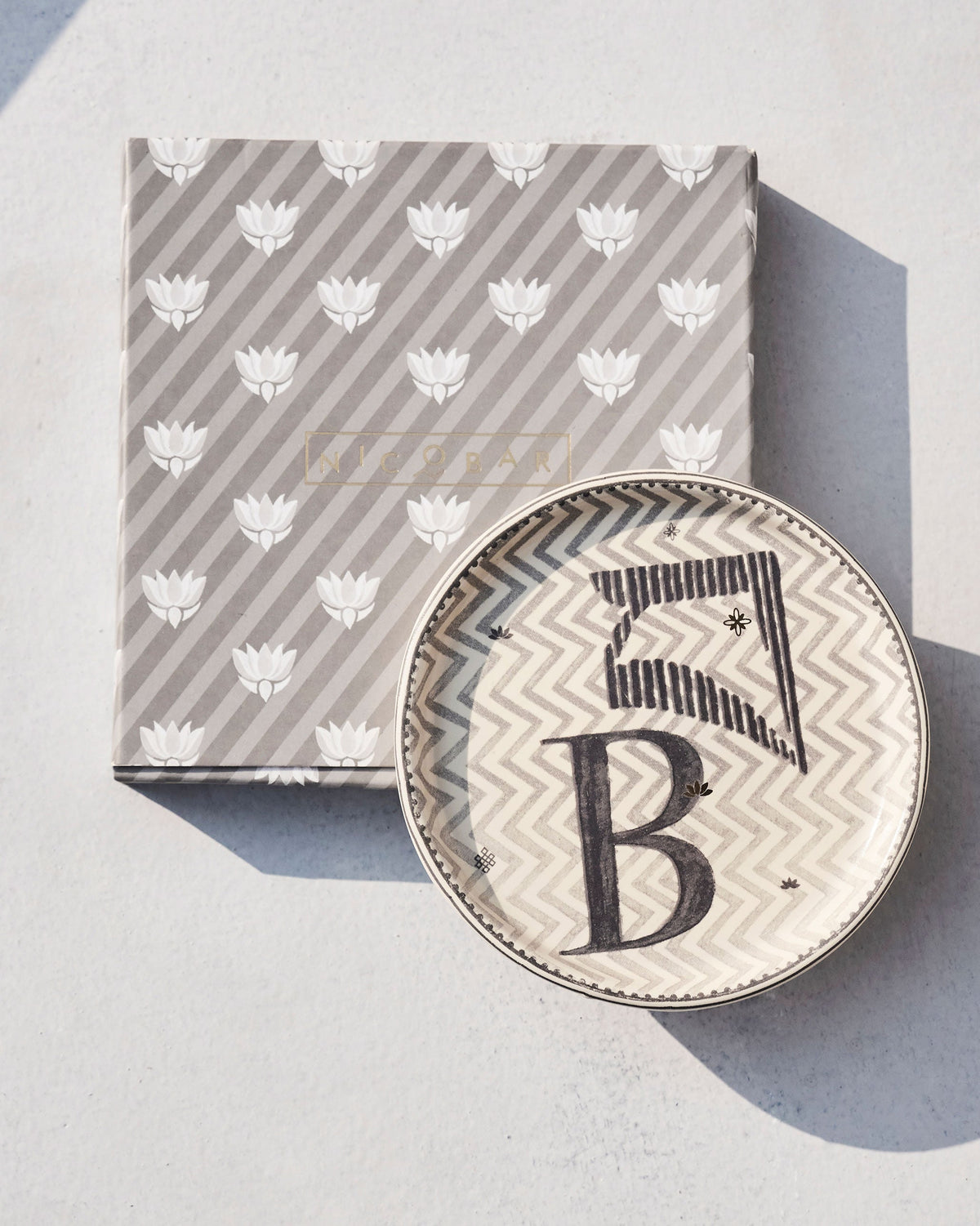 Akshar Coaster resting on its grey lotus-print gift box.