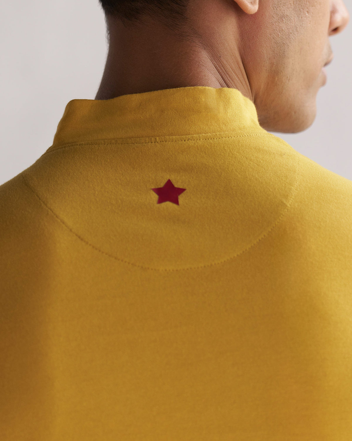 Close-up of the back neck of a mustard turtle neck t-shirt showing a red star embroidery.