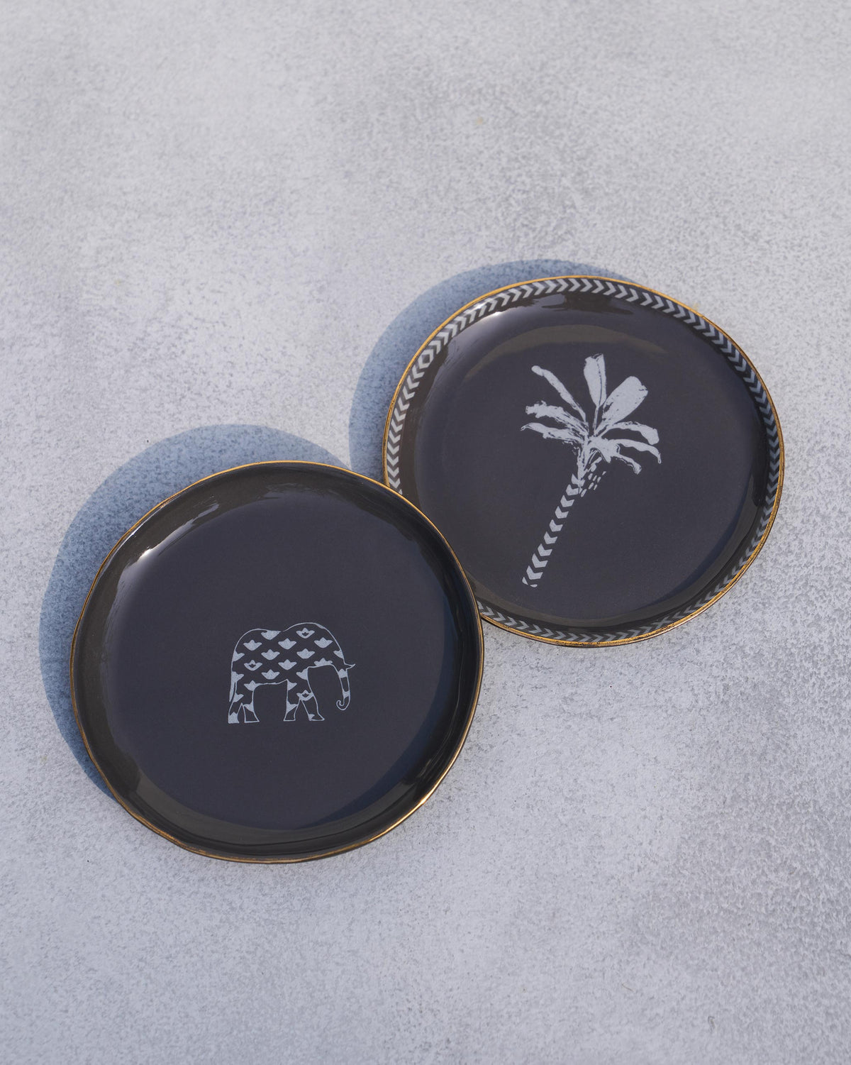 Two Coastal Tea Plates in charcoal, one with a palm motif and a chevron-patterned rim.