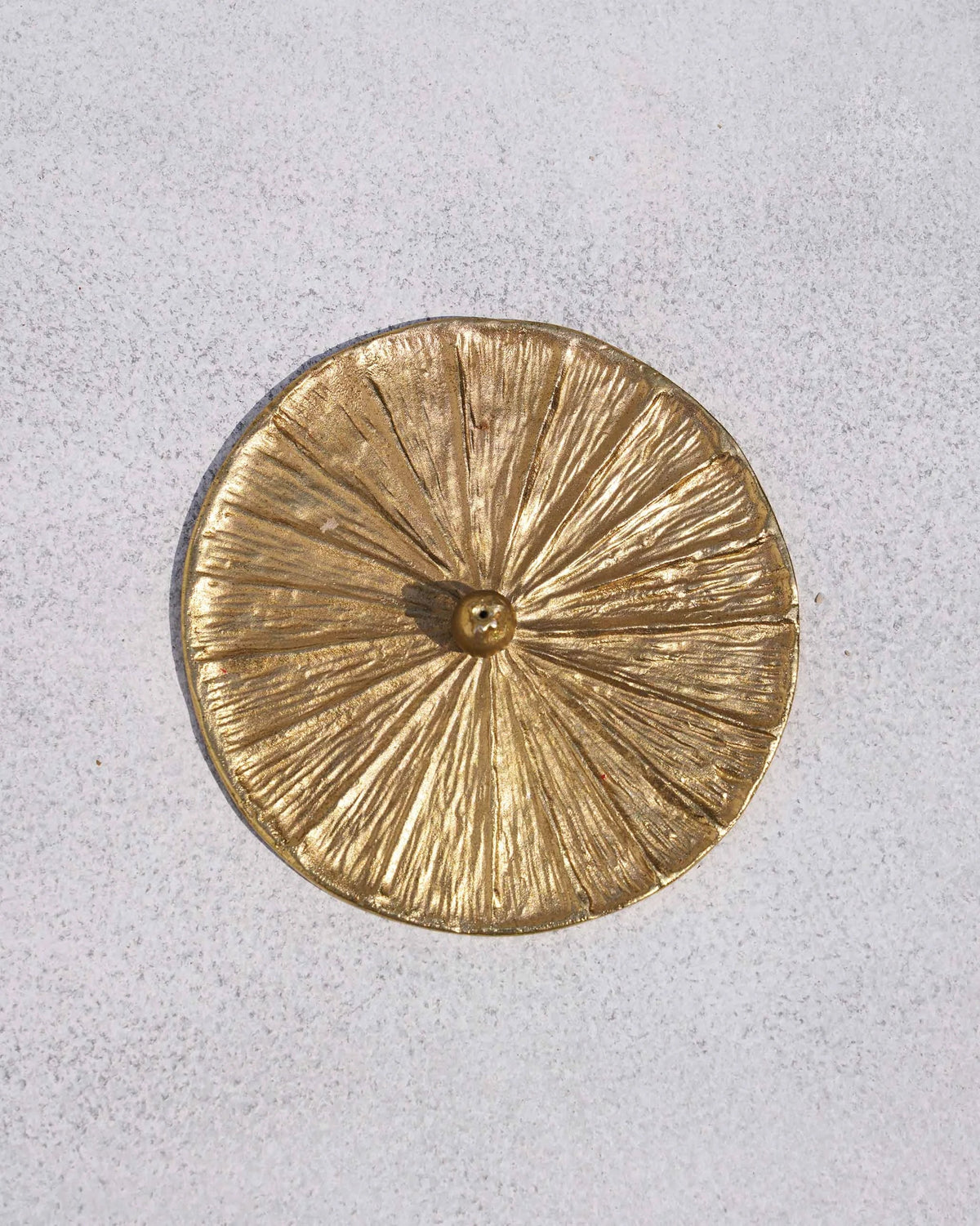 Overhead view of a gold Anar incense holder with a sunburst textured base.